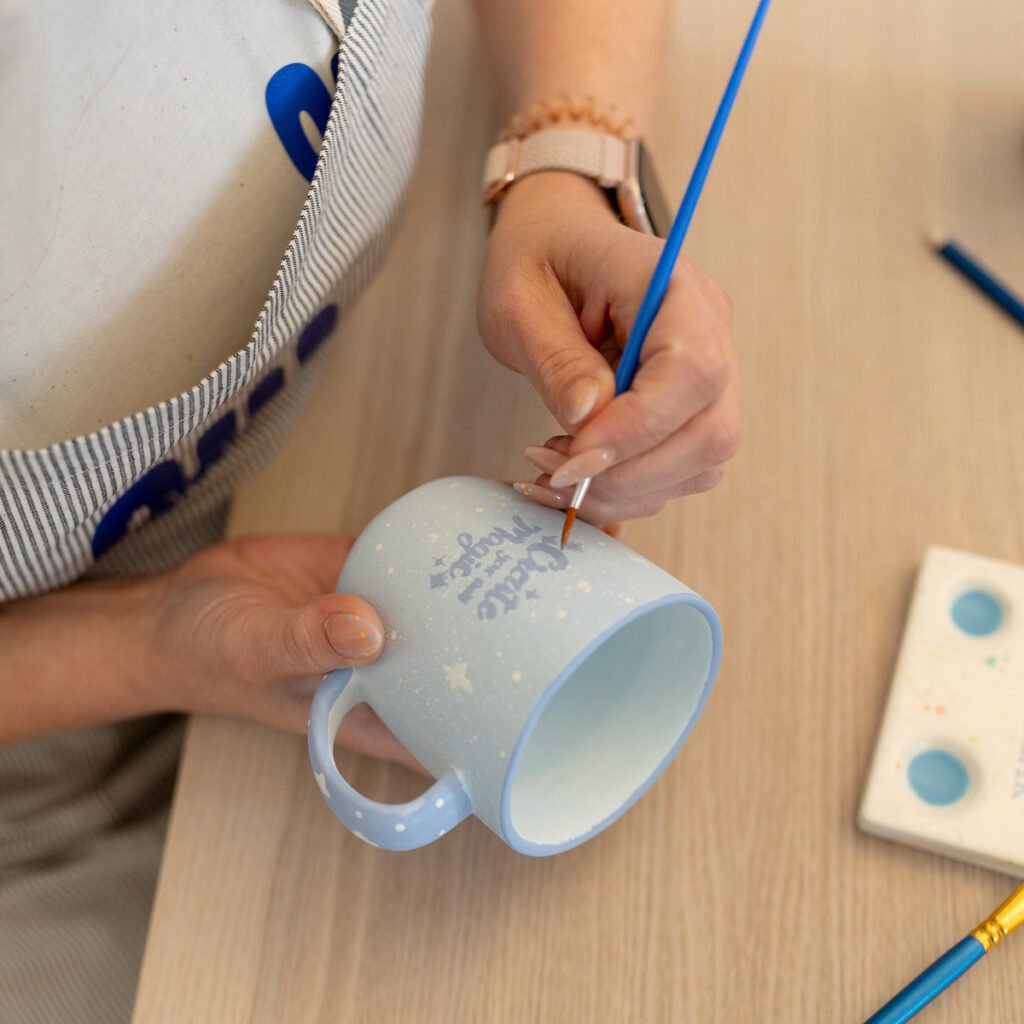 Hände bemalen eine hellblaue Keramiktasse mit feinem Pinsel